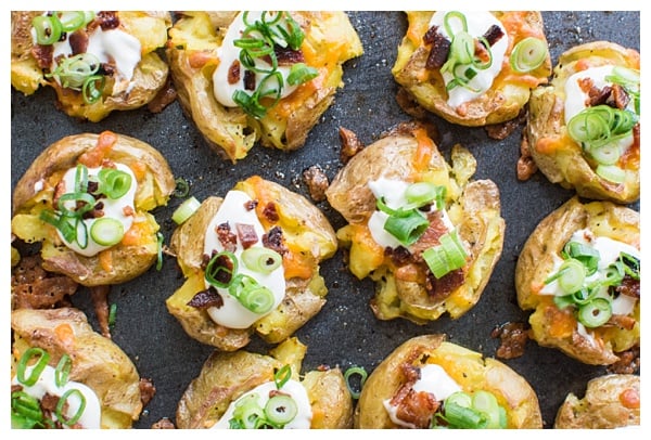 Loaded Smashed Potatoes -- crispy smashed potatoes topped with cheddar cheese, bacon, sour cream, and scallions. A fun side dish or perfect party appetizer!