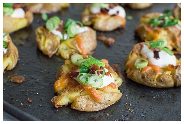 Loaded Smashed Potatoes -- crispy smashed potatoes topped with cheddar cheese, bacon, sour cream, and scallions. A fun side dish or perfect party appetizer!